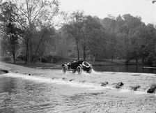 Couple In Automobile Fording A River At A Low Water Crossing Near A Small Stone Bridge, ca.1913-1918 Creator: Harris & Ewing