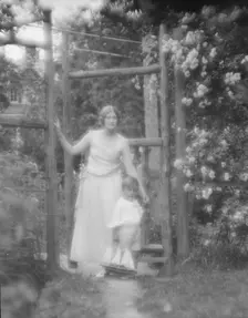 Conroy, Frank, Mrs., and child, standing by a garden gate, 1923 Creator: Arnold Genthe