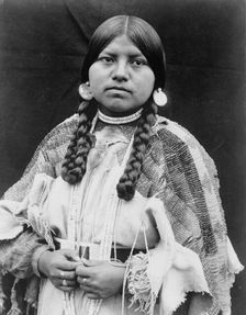 Cayuse woman, half-length portrait, standing, facing front, braids, shell disk earrings..., c1910. Creator: Edward Sheriff Curtis