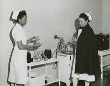 Captain Mary L. Petty, Chief Nurse, holding a glass bottle and showing it to 2nd Lieut..., 1939 - 19 Creator: Unknown