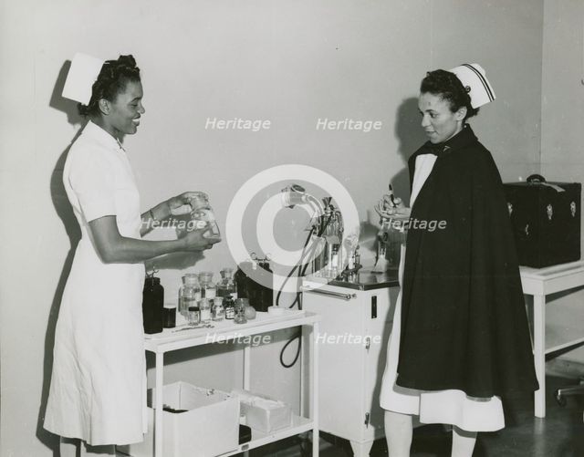 Captain Mary L. Petty, Chief Nurse, holding a glass bottle and showing it to 2nd Lieut..., 1939 - 19 Creator: Unknown.