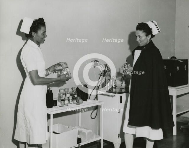 Captain Mary L. Petty, Chief Nurse, holding a glass bottle and showing it to 2nd Lieut..., 1939 - 19 Creator: Unknown.