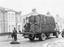 Charringtons delivering sacks of coal down a residential street. Creator: Unknown