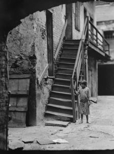 Child standing next to a stairway in a courtyard, New Orleans, between 1920 and 1926. Creator: Arnold Genthe