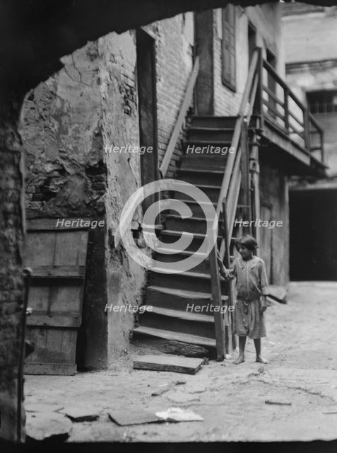 Child standing next to a stairway in a courtyard, New Orleans, between 1920 and 1926. Creator: Arnold Genthe.