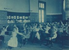 Children doing calisthenics while sitting at their desks in a classroom..., Washington, DC, (1899?). Creator: Frances Benjamin Johnston