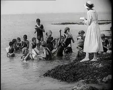 Children Having Swimming Lessons in the Sea While the Teacher Stands on a Rock, 1921. Creator: British Pathe Ltd