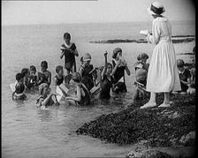 Children Having Swimming Lessons in the Sea While the Teacher Stands on a Rock, 1921. Creator: British Pathe Ltd
