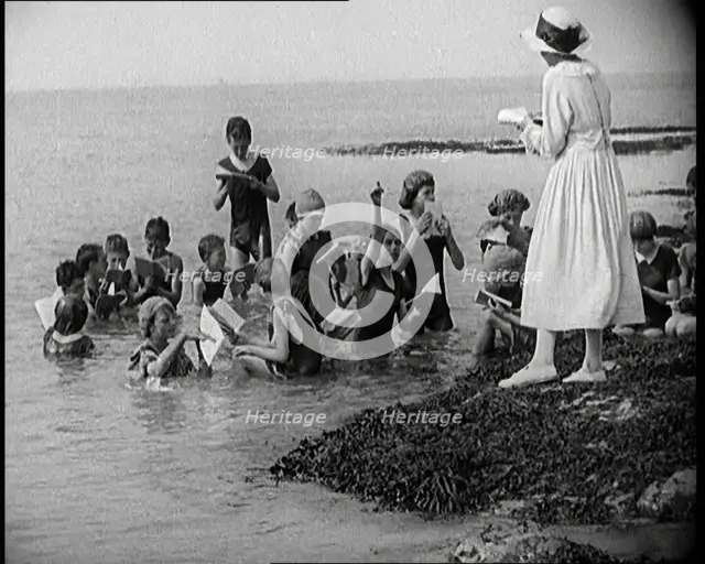 Children Having Swimming Lessons in the Sea While the Teacher Stands on a Rock, 1921. Creator: British Pathe Ltd.