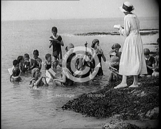 Children Having Swimming Lessons in the Sea While the Teacher Stands on a Rock, 1921. Creator: British Pathe Ltd.