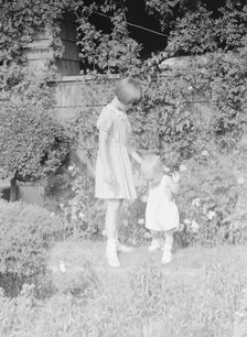 Children of Mrs. George Eustis standing outdoors in a garden, between 1911 and 1942. Creator: Arnold Genthe