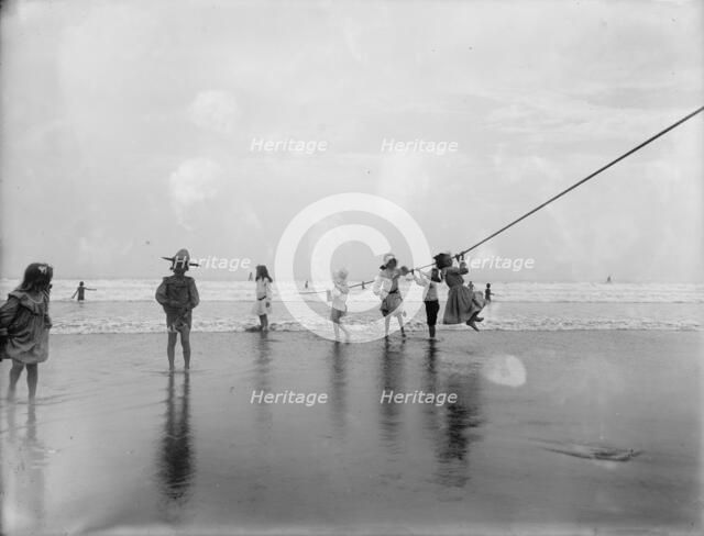 Children swinging on pier rope at beach, between 1900 and 1910. Creator: Unknown.