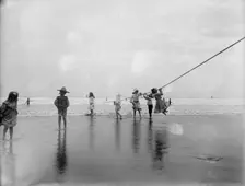 Children swinging on pier rope at beach, between 1900 and 1910. Creator: Unknown