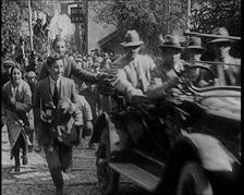 Crowd Chasing a Motorcar as It Climbs up a Hilly Cobbled Street, 1920. Creator: British Pathe Ltd