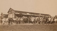 Crowds of people in front of buildings at the marketplace in the center of town..., (1899?). Creator: Eleanor Lord Pray