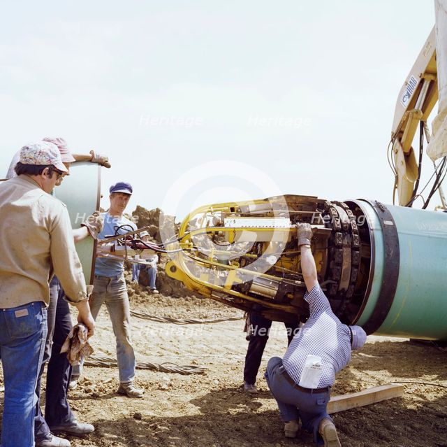 A team of men joining two steel pipes together on the Martin pipeline, Hertfordshire, 07/07/1981. Creator: John Laing plc.