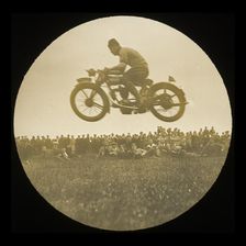 A view of a motorcycle jumping in front of a crowd of onlookers at an unknown..., 1920s-1930s. Creator: Norman Kingsley Harrison