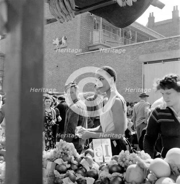 A woman buys fruit at a stall in a North London street market, c1946-c1959. Artist: John Gay