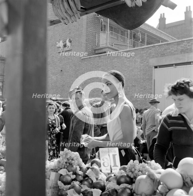 A woman buys fruit at a stall in a North London street market, c1946-c1959. Artist: John Gay