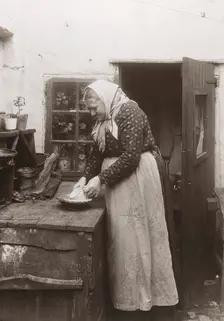 A woman in apron and headscarf washing up a mug outside her home, Landskrona, Sweden, 1910. Creator: Unknown
