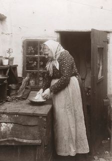 A woman in apron and headscarf washing up a mug outside her home, Landskrona, Sweden, 1910. Creator: Unknown