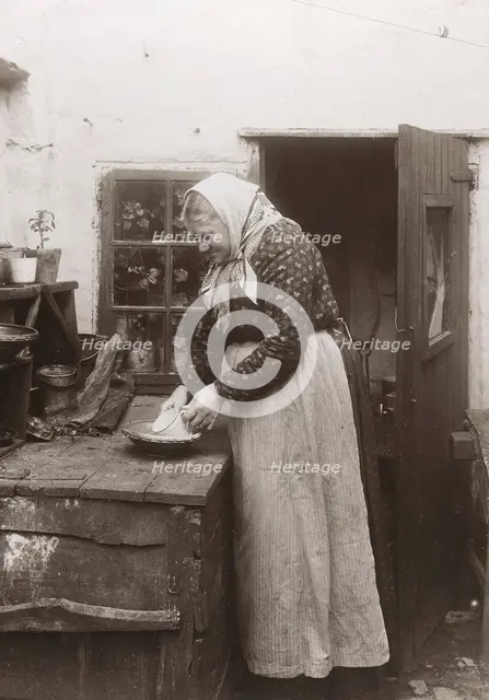 A woman in apron and headscarf washing up a mug outside her home, Landskrona, Sweden, 1910. Creator: Unknown.