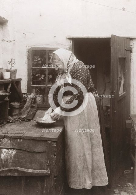 A woman in apron and headscarf washing up a mug outside her home, Landskrona, Sweden, 1910. Creator: Unknown.