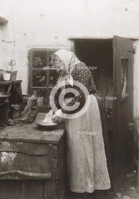 A woman in apron and headscarf washing up a mug outside her home, Landskrona, Sweden, 1910. Artist: Unknown