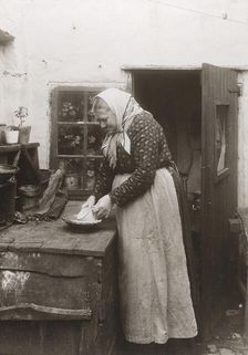 A woman in apron and headscarf washing up a mug outside her home, Landskrona, Sweden, 1910