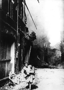 A woman leaving her burning house in a bombed street, Germany, 1945