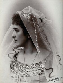 A woman posing in a photographic studio, wearing a bridal? dress and veil, in front of..., 1900-1910 Creator: Unknown