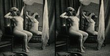 A woman posing naked in a photographic studio, sitting on a chair in front of a looking-glass, c1900 Creator: Unknown
