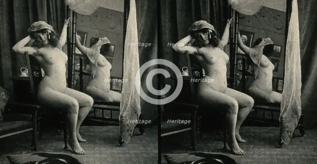 A woman posing naked in a photographic studio, sitting on a chair in front of a looking-glass, c1900 Creator: Unknown.
