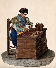 A woman sits at a wooden box counting money out of a basket onto a tray. Creator: Unknown