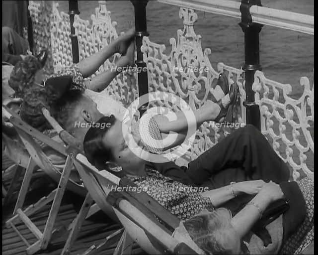 A Woman Sleeping in a Deckchair by Railings on the Promenade at Brighton With a Man and..., 1939. Creator: British Pathe Ltd.