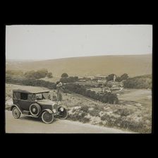 A woman standing beside a car parked on East Dean Road near Exceat Hill, looking out..., 1921-1939. Creator: Norman Kingsley Harrison