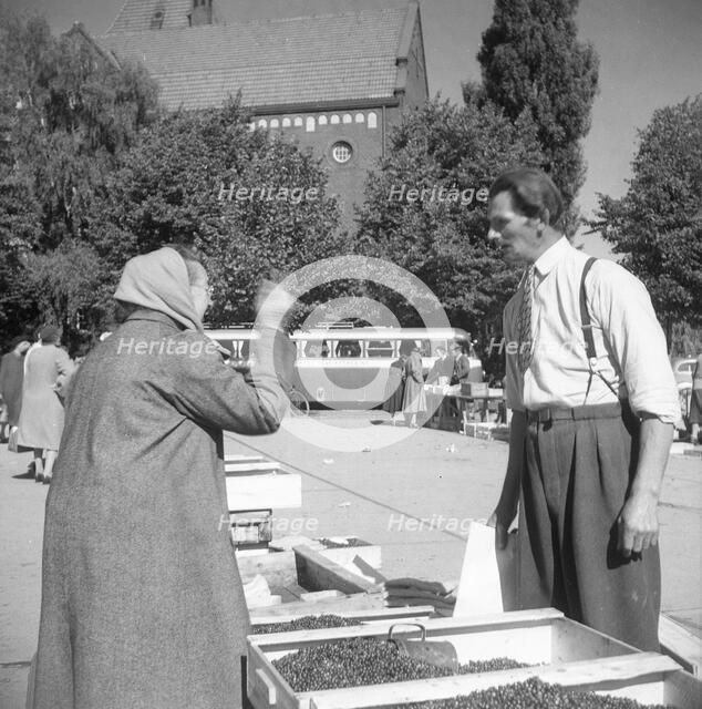 A women buying lingonberries in the market square, Landskrona, Sweden, 1952. Artist: Unknown