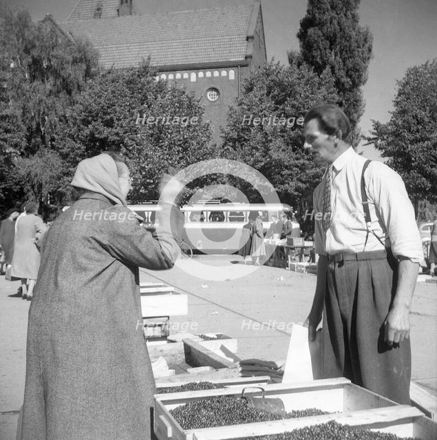 A women buying lingonberries in the market square, Landskrona, Sweden, 1952. Creator: Unknown.