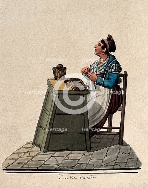 A women is sitting knitting at a table in the street with money on it in trays. Creator: Unknown.