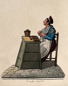 A women is sitting knitting at a table in the street with money on it in trays. Creator: Unknown