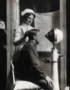 A young uniformed man sitting with a pillow on his chair, facing a machine..., c1910s. Creator: Unknown