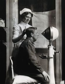A young uniformed man sitting with a pillow on his chair, facing a machine..., c1910s. Creator: Unknown