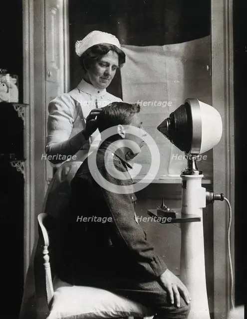 A young uniformed man sitting with a pillow on his chair, facing a machine..., c1910s. Creator: Unknown.