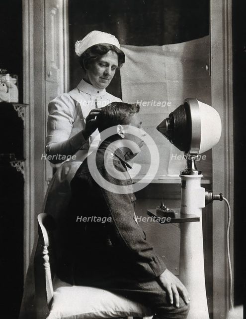 A young uniformed man sitting with a pillow on his chair, facing a machine..., c1910s. Creator: Unknown.