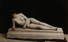 A young woman posing naked in a photographic studio, lying on a wooden plinth, approx 1900. Creator: Unknown