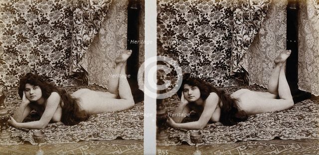 A young woman posing naked in a photographic studio, lying on her front on a piece of..., c1900. Creator: Unknown.