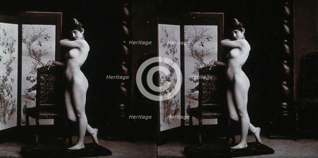 A young woman posing naked in a photographic studio, leaning on the back of a chair..., c1900. Creator: Unknown.