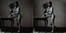 A young woman posing naked in a photographic studio, standing in front of a table on which..., c1900 Creator: Unknown