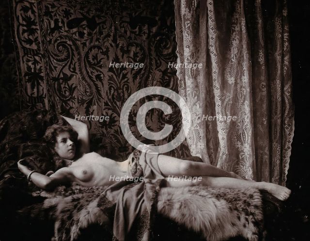 A young woman, posing semi-naked in a photographic studio, lying full-length on a fur..., c1900. Creator: Unknown.