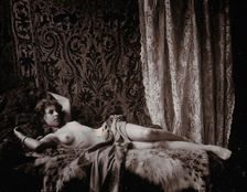 A young woman, posing semi-naked in a photographic studio, lying full-length on a fur..., c1900. Creator: Unknown